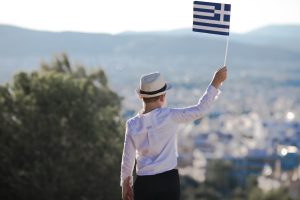smiling-baby-toddler-boy-holding-greece-flag-city-background-independence-day-flag-day